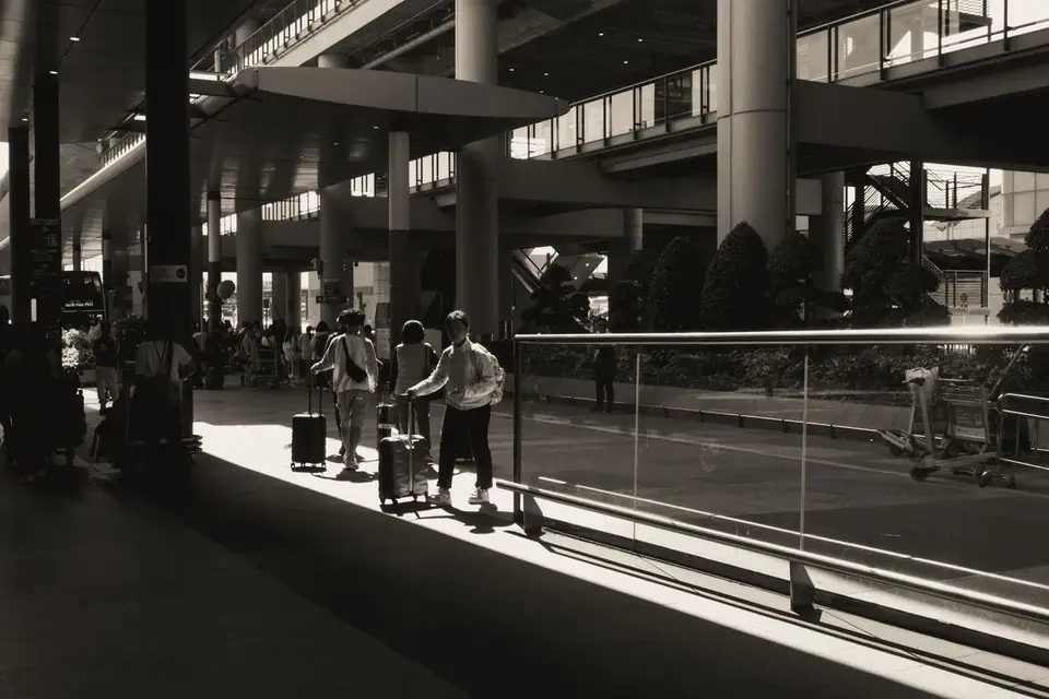 Silhouettes de voyageurs et de leurs bagages dans un hall d'aéroport baigné de lumière