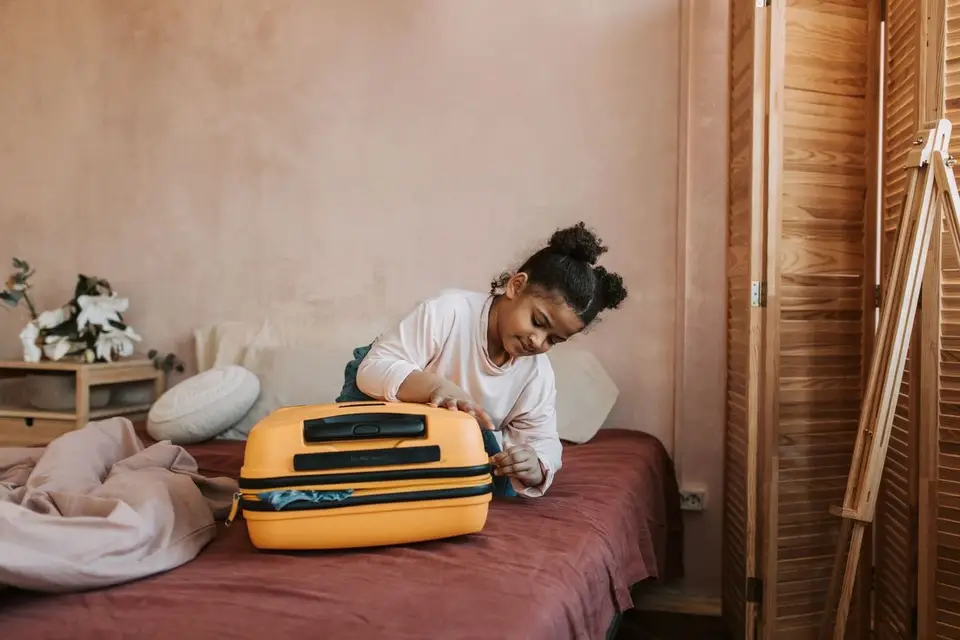 Enfant fermant sa valise posée sur un lit avant le départ