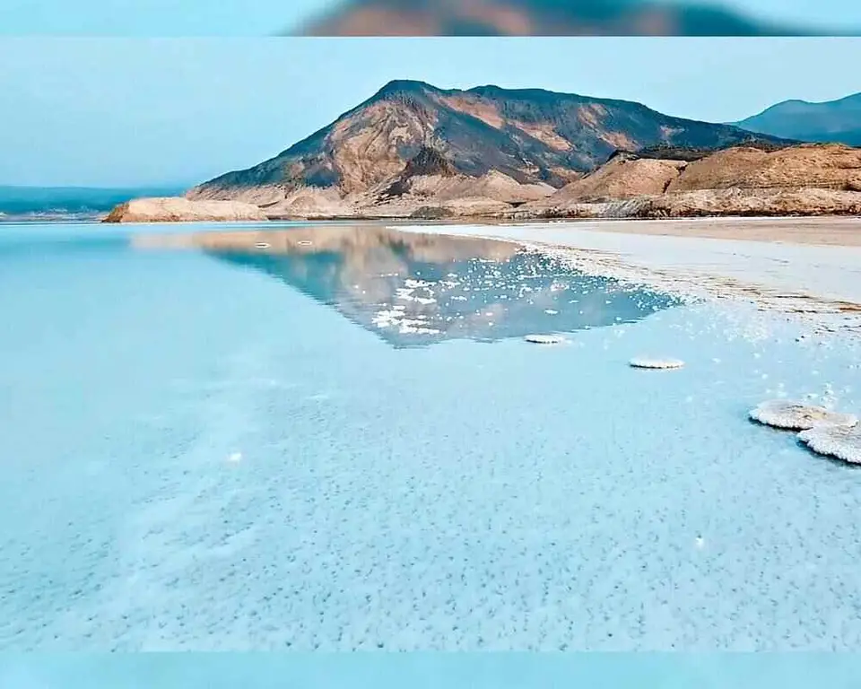 White salt flats of Lake Assal bordered by black volcanic rock under a clear blue sky